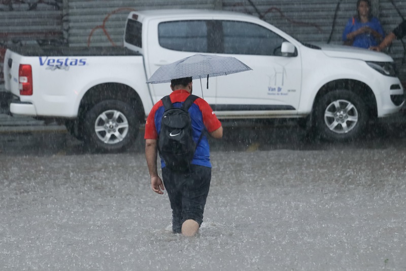 Homem caminha na chuva, em área alagada, em alusão ao alerta do Inmet